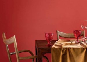 Dining room with coral tinged with pink painted wall, a table, chairs, cups and a branch with buds