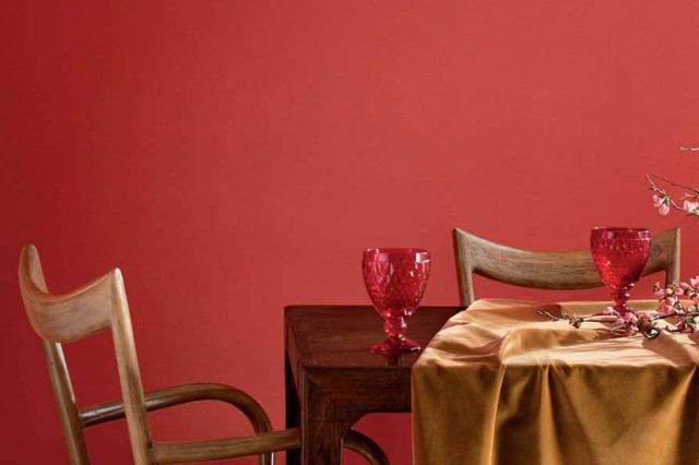 Dining room with coral tinged with pink painted wall, a table, chairs, cups and a branch with buds